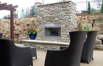 A backyard patio with an outdoor fireplace and chairs.