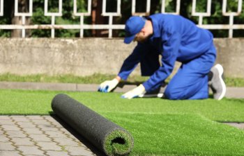 Young man in uniform installing artificial turf outdoors, selective focus